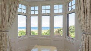 A room with a bay window overlooking a beach, a small table, and cream-colored curtains. - A unique, spectacular detached home in a much sought-after area with unbeatable panoramic sea views. (North Berwick)