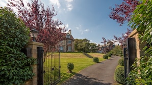 A gated driveway leading to a house with a stone wall and a lamp post. - A unique, spectacular detached home in a much sought-after area with unbeatable panoramic sea views. (North Berwick)