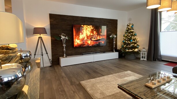 A modern living room with a flat-screen TV mounted on a wooden wall, a glass coffee table, a Christmas tree, and a fireplace. - NEW 5 star holiday comfort apartment (Braunlage)