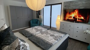 A modern bedroom with a large bed, a fireplace, and a view of the outdoors. - NEW 5 star holiday comfort apartment (Braunlage)