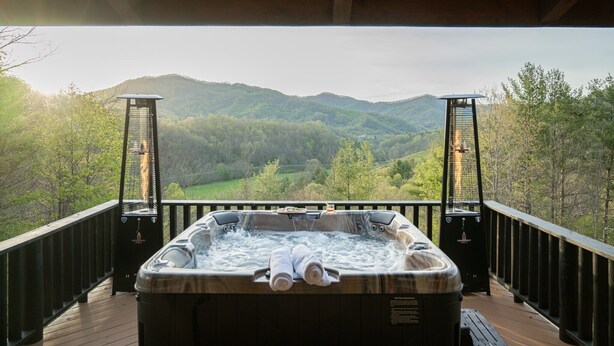 Ein Whirlpool auf einer Holzterrasse mit Blick auf ein bewaldetes Tal und Hügel.