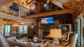 Eine großzügige Lodge mit Kamin aus Stein, einem darüber montierten Fernseher und einer gemütlichen Sitzecke mit Ledersofas und einem Esstisch.