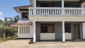 Ein zweistöckiges Gebäude mit Balkon, Satellitenschüssel und einem gepflasterten Eingangsbereich.