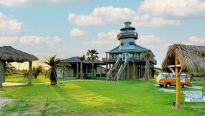 A coastal house with a tower, a thatched-roof structure, and a vintage van.