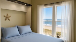 A bedroom with a bed, a starfish decoration, and a view of the beach through sheer curtains.