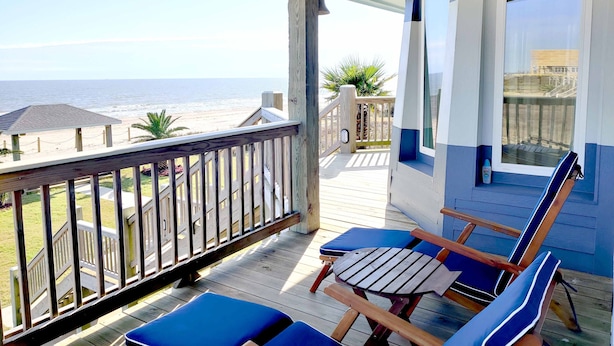 A wooden deck with a view of the ocean, a small covered area, and two blue chairs.