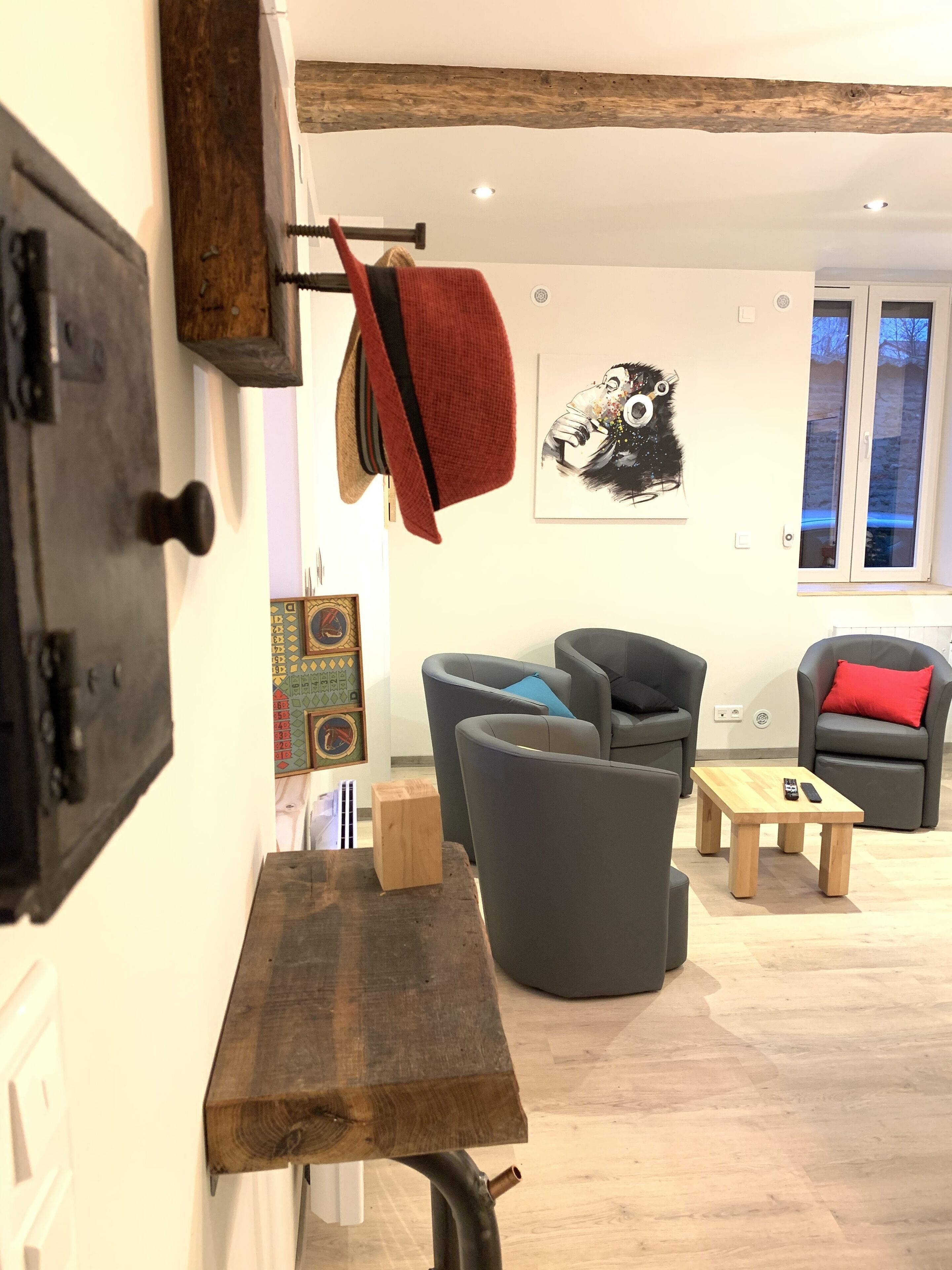 A modern living room with a wooden table, grey armchairs, and a red throw blanket hanging on a hook.