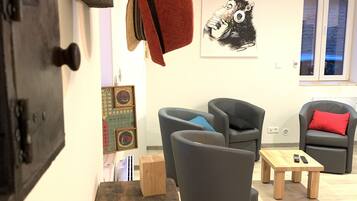 A modern living room with a wooden table, grey armchairs, and a red throw blanket hanging on a hook.