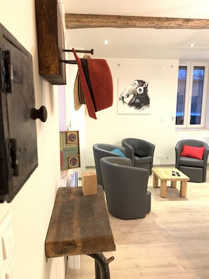 A modern living room with a wooden table, grey armchairs, and a red throw blanket hanging on a hook.