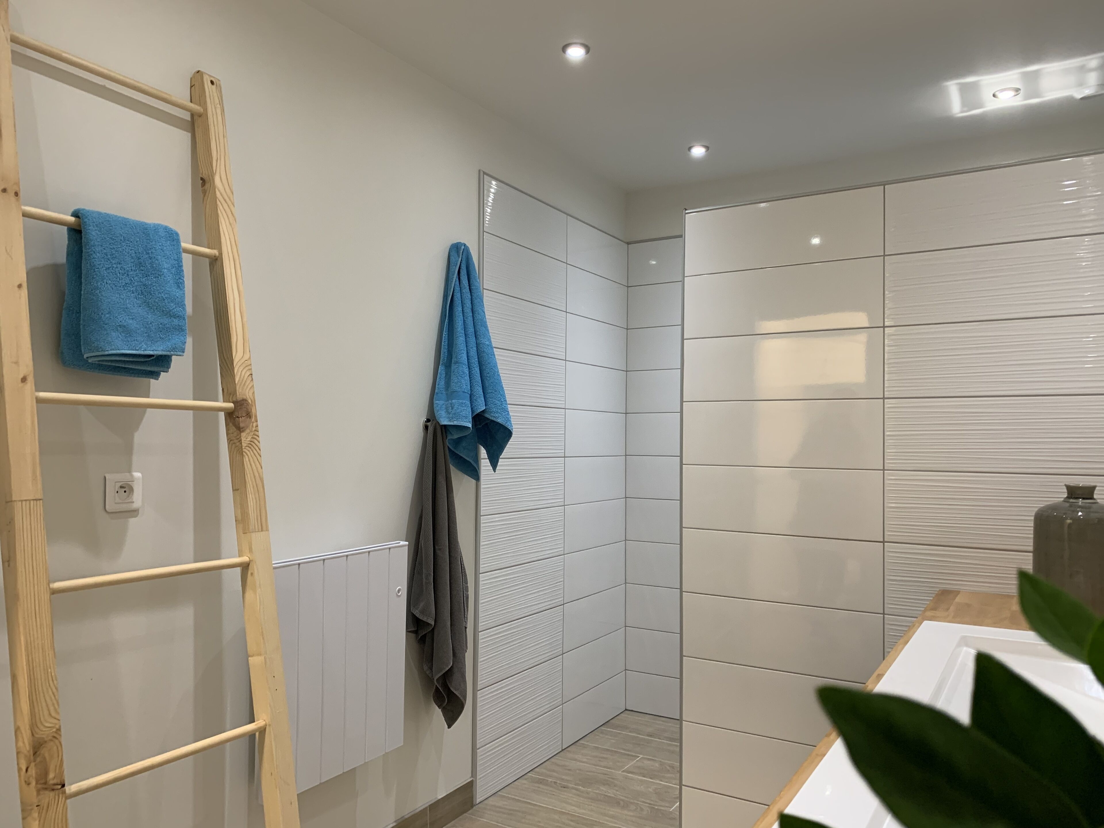 A modern bathroom with a wooden ladder, tiled walls, and a white sink.