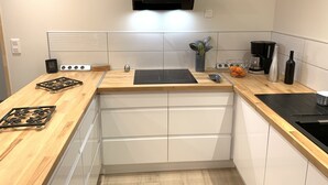 A modern kitchen with a wooden countertop, a built-in stove, a coffee maker, and a clock on the wall. - Gîte Le BISTANCLAC in the heart of the town of CHARLIEU. (Charlieu)