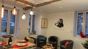 A modern living room with a dining area, featuring a wooden table set for a meal, comfortable seating, and large windows with a view. - Gîte Le BISTANCLAC in the heart of the town of CHARLIEU. (Charlieu)