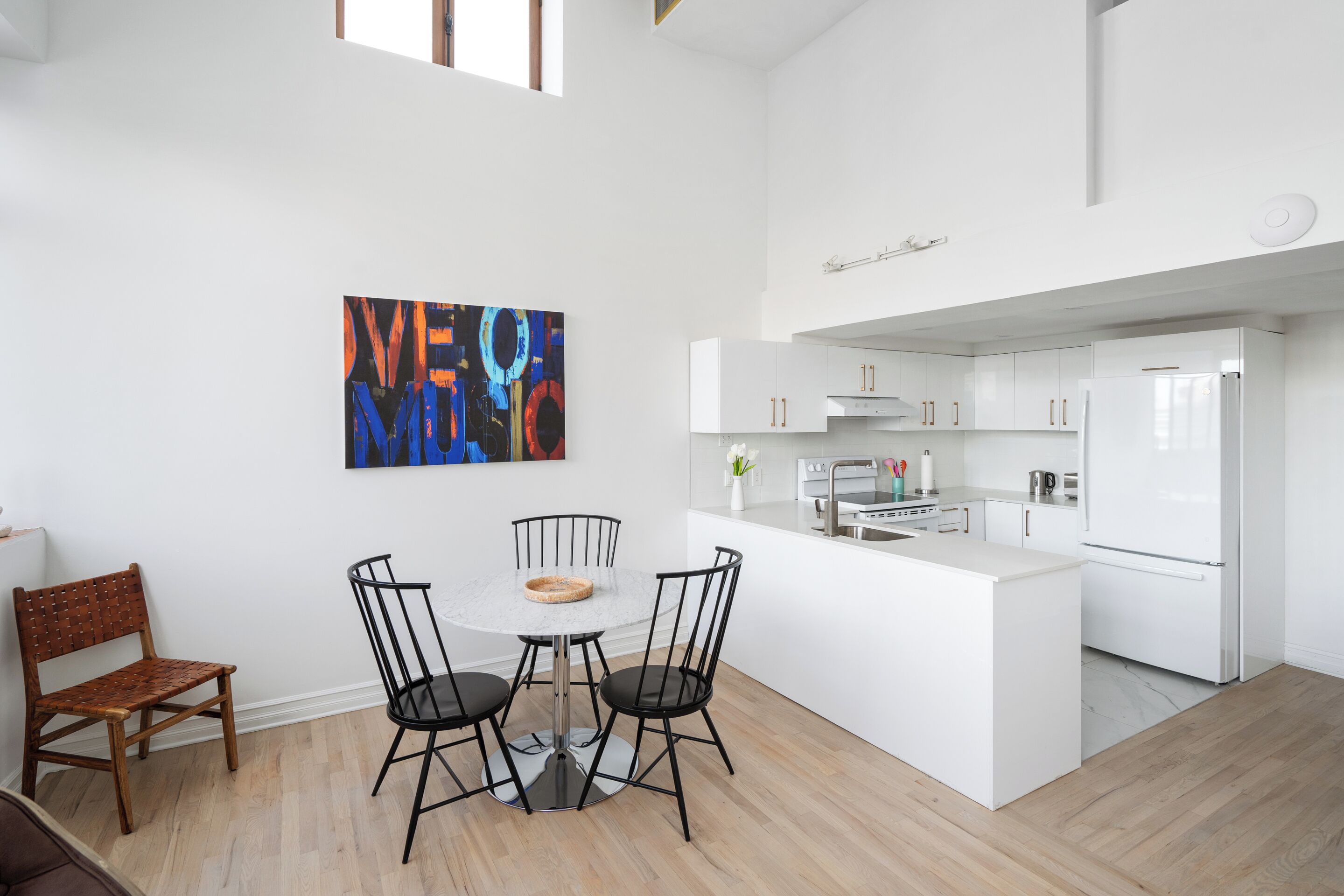 A modern kitchen with white cabinetry, a central island, and a dining area with a round table and four chairs.