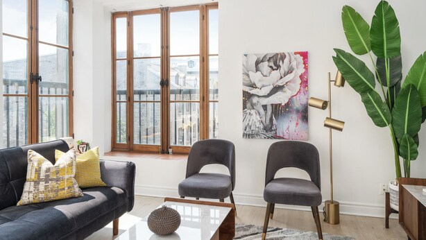 A modern living room with a sofa, two chairs, a coffee table, a floor lamp, and a large plant. - Le Nomade MTL (Montreal)