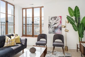 Ein modernes Wohnzimmer mit einer Couch, zwei Sesseln, einem Couchtisch, einer Stehlampe und einer großen Pflanze.