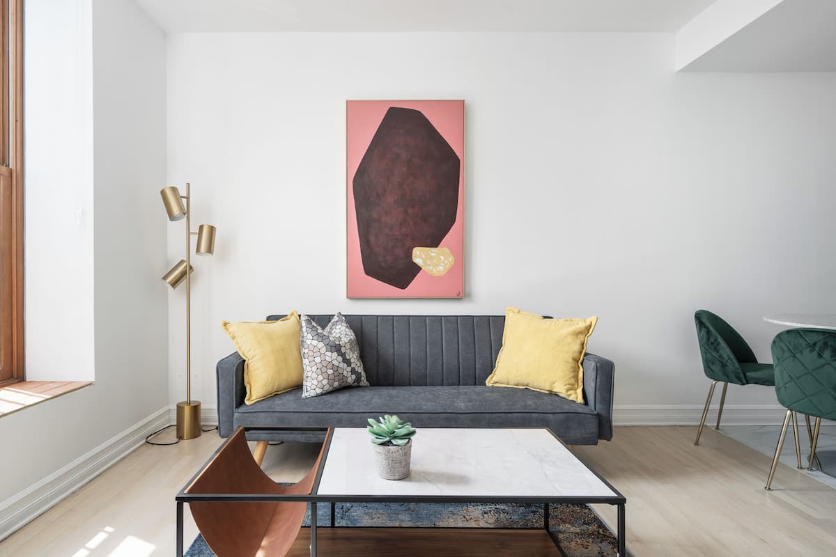 A modern living room with a grey sofa, yellow and patterned cushions, a coffee table with a plant, and a floor lamp.