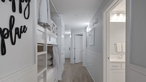 Un pasillo con un armario blanco, una cama tipo altillo y un baño con lavabo y perchero.