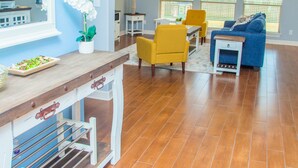 Ein geräumiges Wohnzimmer mit Holzboden, einem blauen Sofa, gelben Sesseln und einem Essbereich mit weißem Tisch und Stühlen.