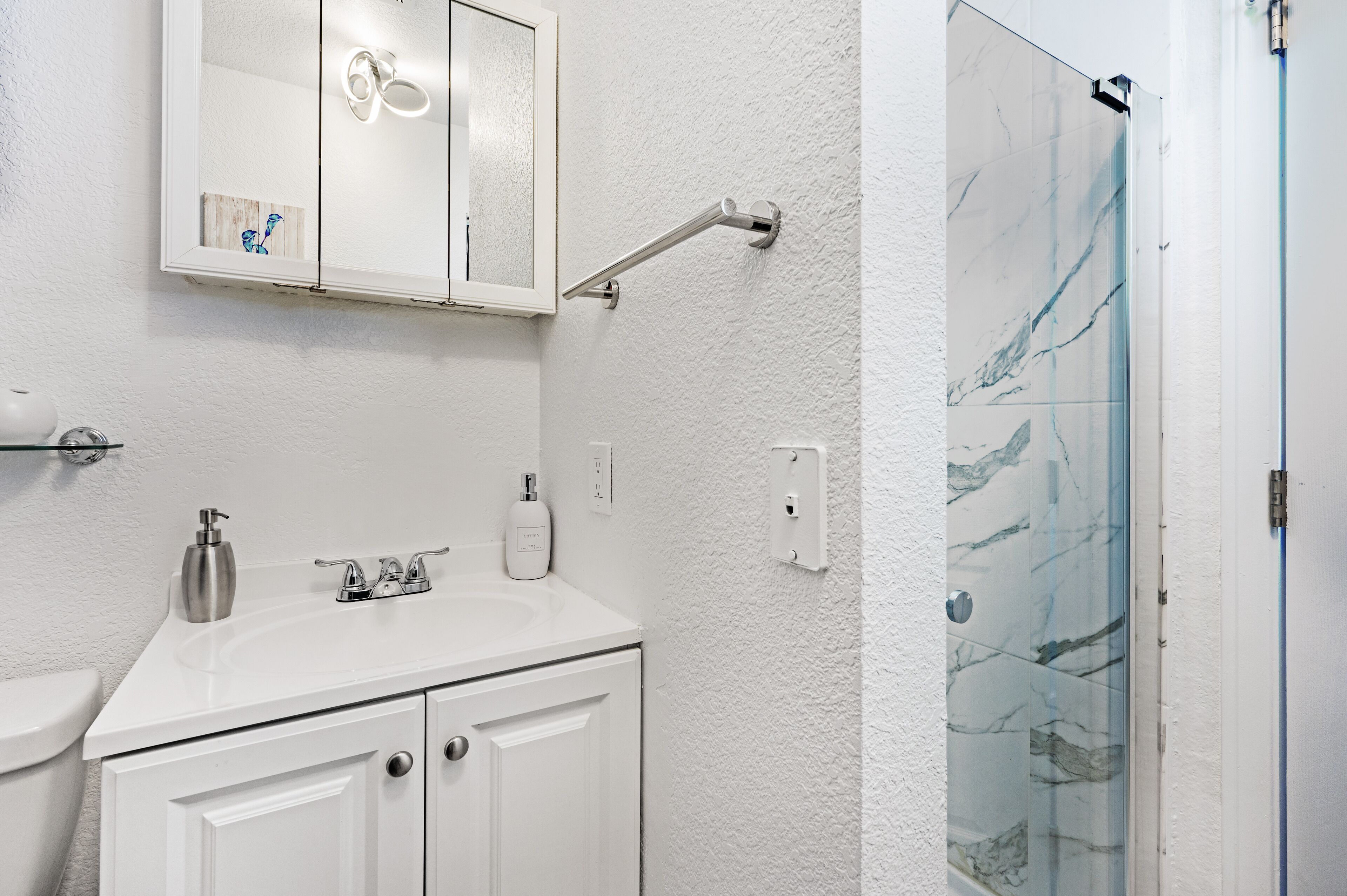 A bathroom with a white sink, a mirror above it, and a glass shower door.