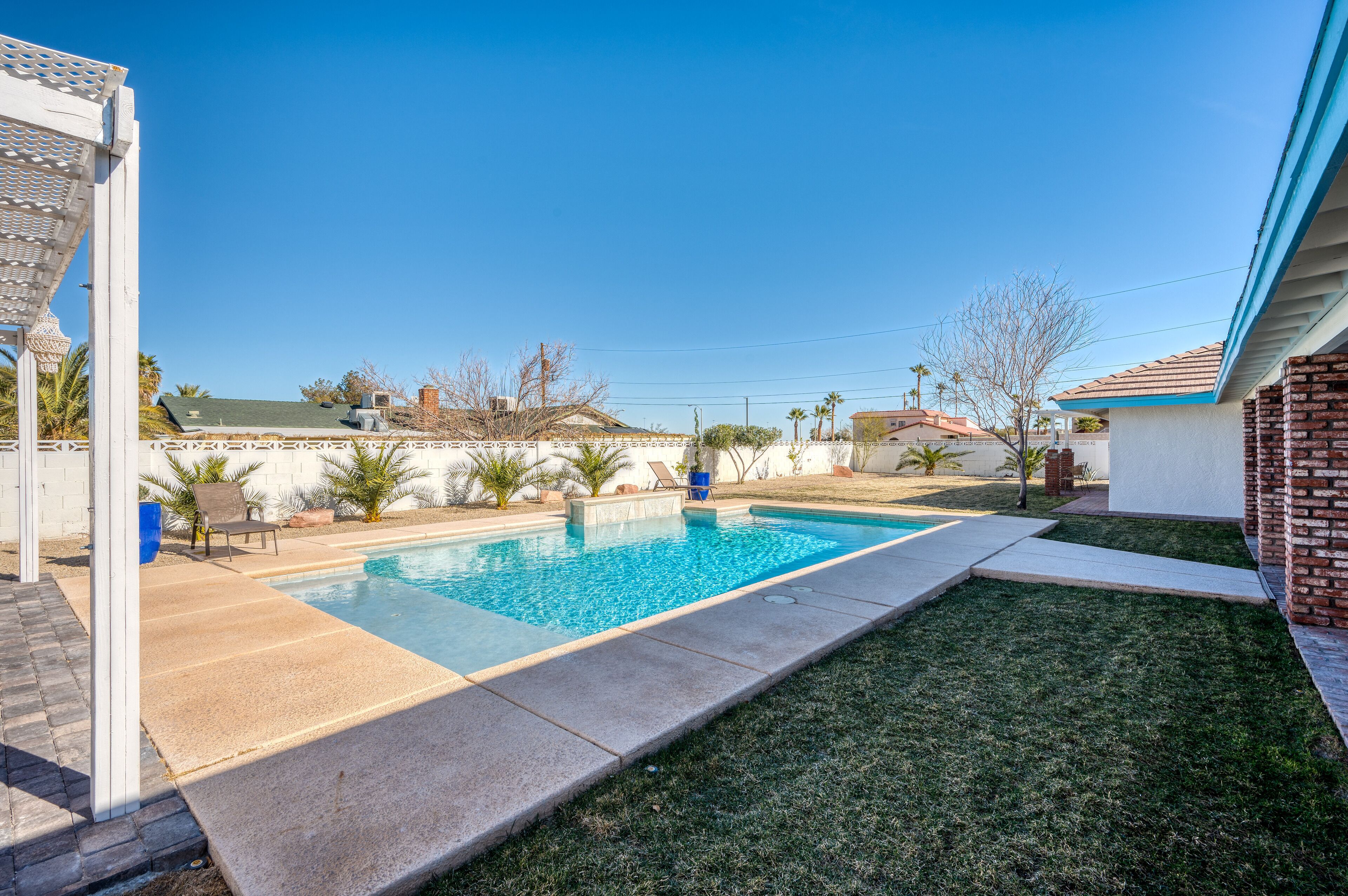 A backyard with a swimming pool, a patio area, and a small lawn.