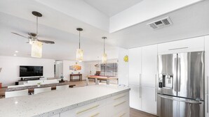 A modern kitchen with a large island, stainless steel appliances, pendant lighting, and a ceiling fan. - Las Vegas Dream House with Backyard Oasis (Henderson)