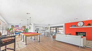 A modern living room with a pool table, a red brick accent wall, and a fireplace. - Las Vegas Dream House with Backyard Oasis (Henderson)