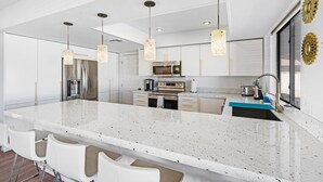 A modern kitchen with white cabinetry, a large island with bar seating, stainless steel appliances, and pendant lighting. - Las Vegas Dream House with Backyard Oasis (Henderson)