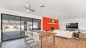 A modern living room with a dining area, a red accent wall, a large TV, and a view of a swimming pool. - Las Vegas Dream House with Backyard Oasis (Henderson)