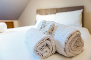 A neatly made bed with rolled towels and toiletries. - Mountsorrel House (Loughborough)