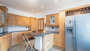 A modern kitchen with wooden cabinets, a stainless steel refrigerator, and a bar stool. - Mountsorrel House (Loughborough)