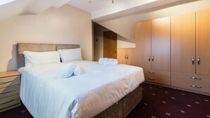 A neatly made bed with white linens, a wooden headboard, and a wooden wardrobe with multiple drawers. - Mountsorrel House (Loughborough)