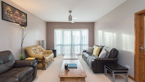 A living room with a brown leather sofa, a yellow leather armchair, a wooden coffee table, and a ceiling fan. - Mountsorrel House (Loughborough)