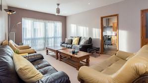 A spacious living room with leather sofas, a wooden coffee table, and a view into the kitchen. - Mountsorrel House (Loughborough)