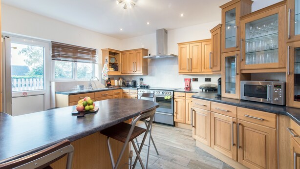 A modern kitchen with wooden cabinets, a central island, stainless steel appliances, and a large window. - Mountsorrel House (Loughborough)