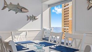 A dining area with white chairs, blue placemats, and a glass table. There are two fish decorations on the wall. - Fall Dates Available! Book Now! Great Location! (Panama City Beach)