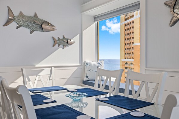 A dining area with white chairs, blue placemats, and a glass table. There are two fish decorations on the wall.