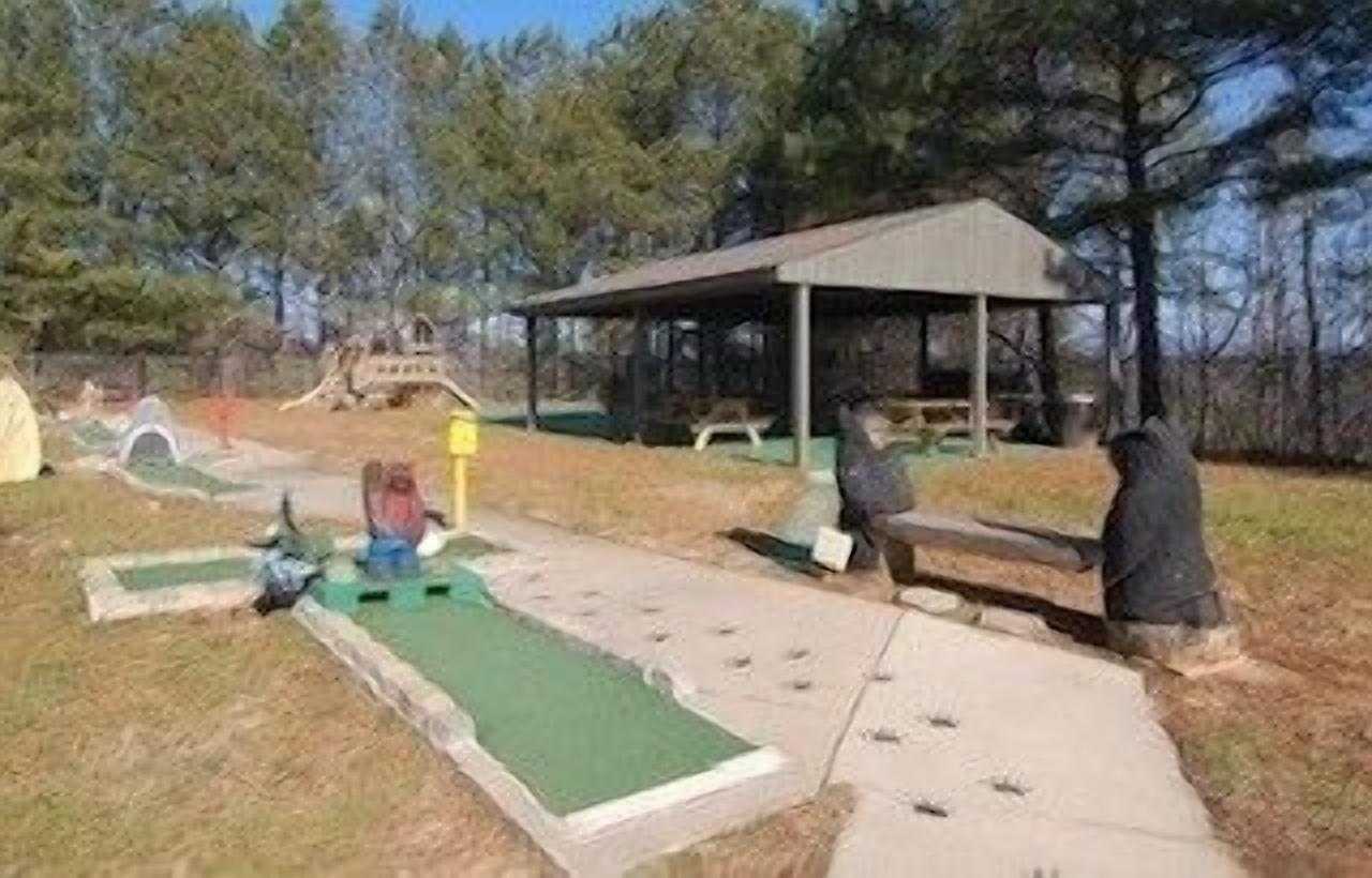 A golf course with a putting green, a covered pavilion, and a bridge.