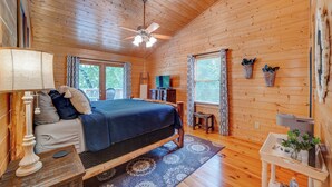 Un dormitorio acogedor estilo cabaña de madera, con cama, escritorio, lámpara y ventilador de techo.