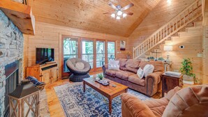 A cozy living room with a stone fireplace, wooden ceiling, and a staircase. - Cozy Family Riverfront Cabin- Hot Tub + Firepit + Apple Orchards + Wineries (Ellijay)