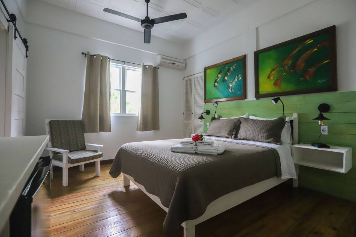 Un dormitorio con cama, una silla, una mesita de noche y dos cuadros en la pared.