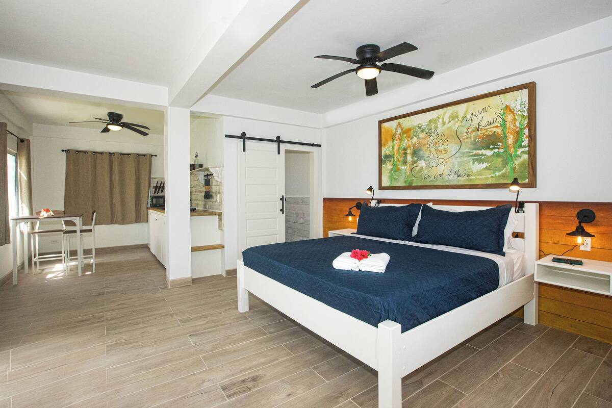 Un dormitorio con cama, escritorio, silla, ventilador de techo y un cuadro en la pared.