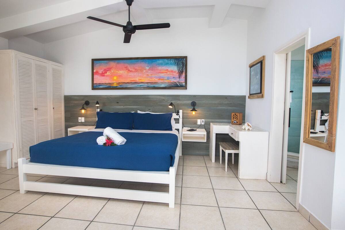 Un dormitorio con cama, mesitas de noche, un escritorio y un ventilador de techo.