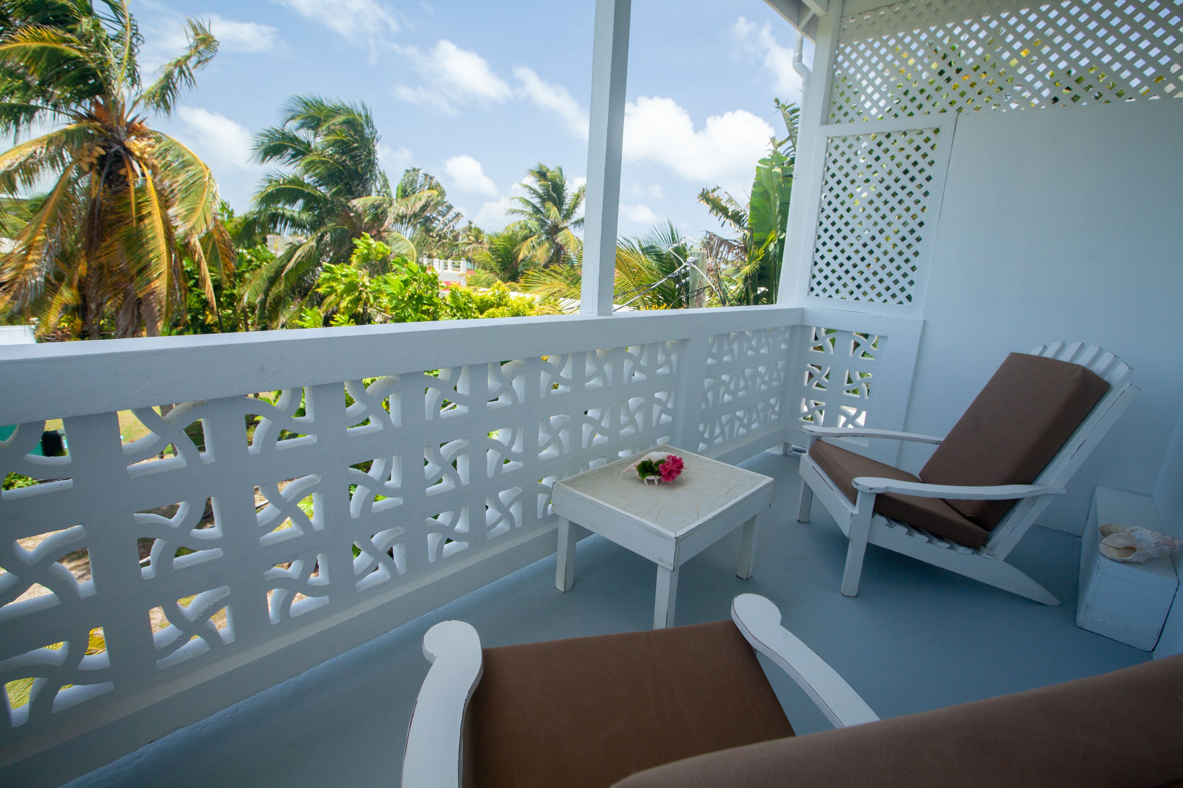 A balcony with white lattice railings, a white table with a flower, and a brown lounge chair.