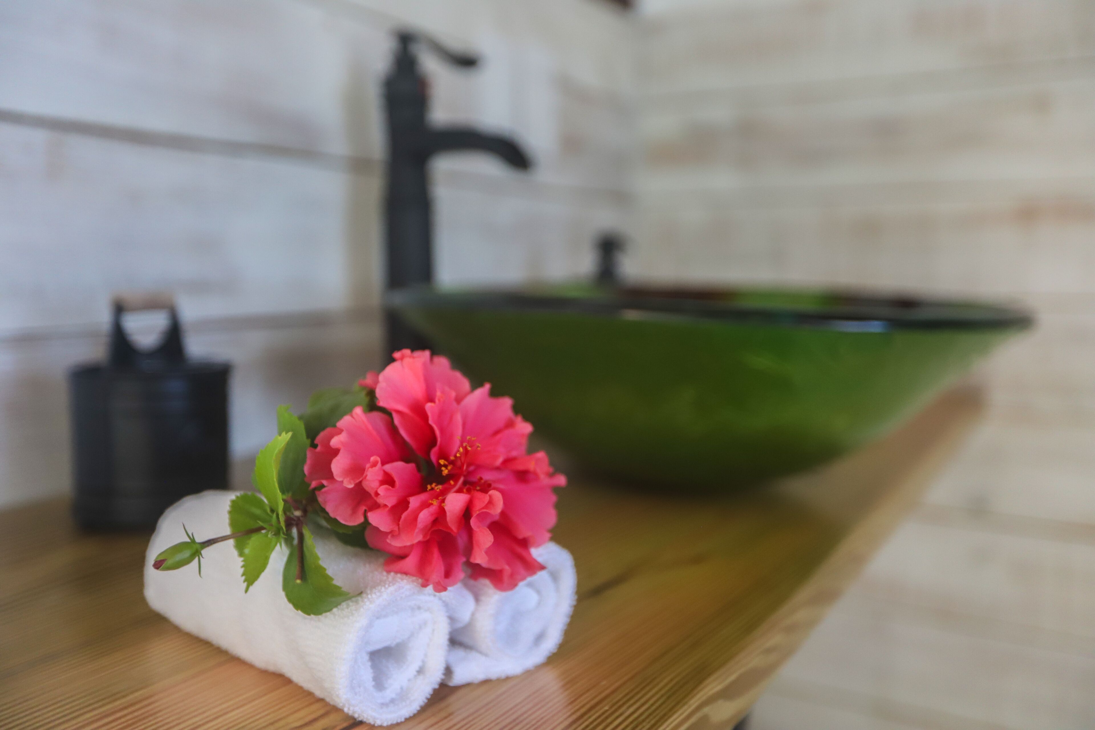 A bathroom with a wooden countertop, a green basin, a towel, and a pink flower.