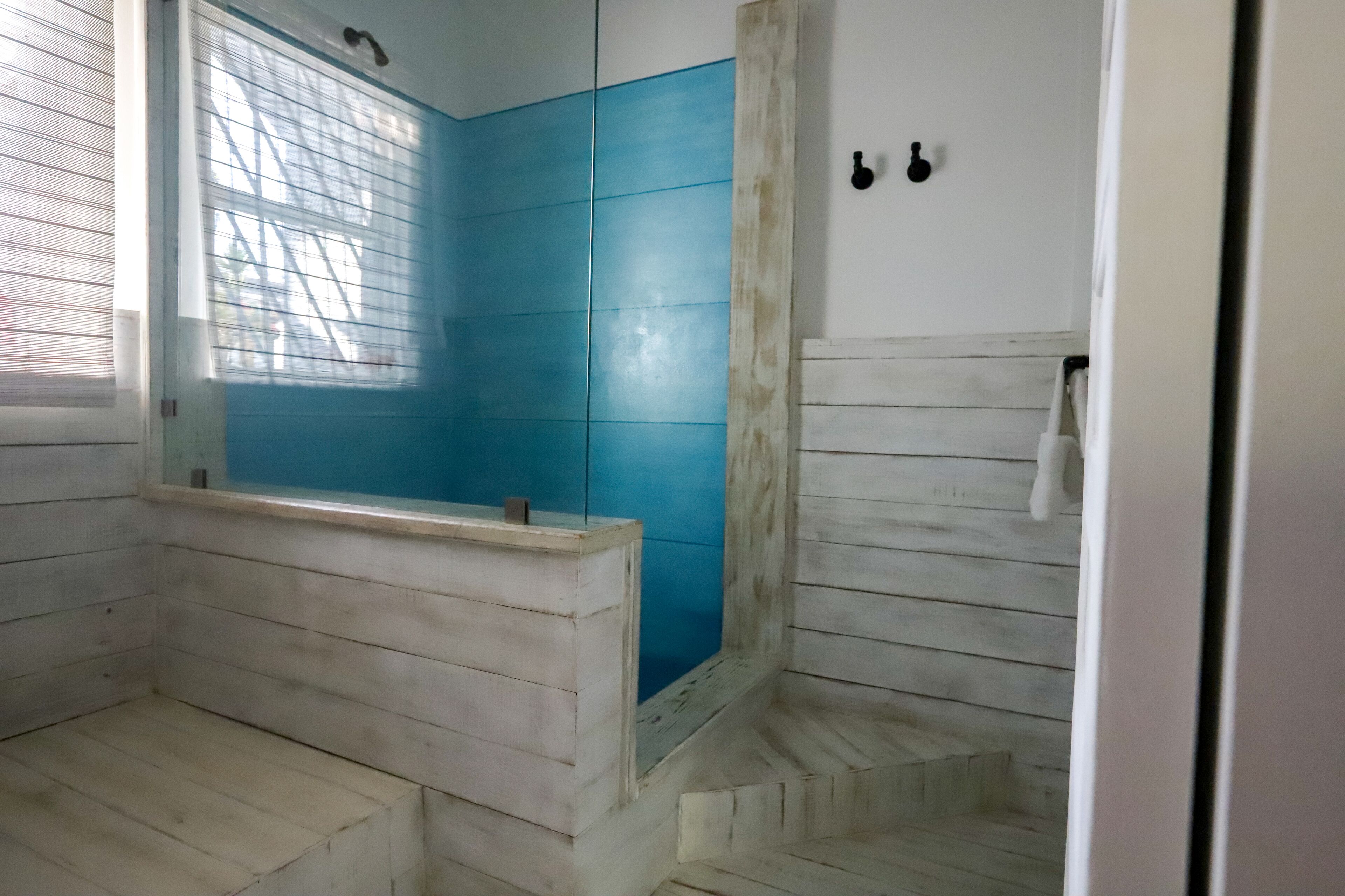 A bathroom with a bathtub, a shower area, and a window with blinds.