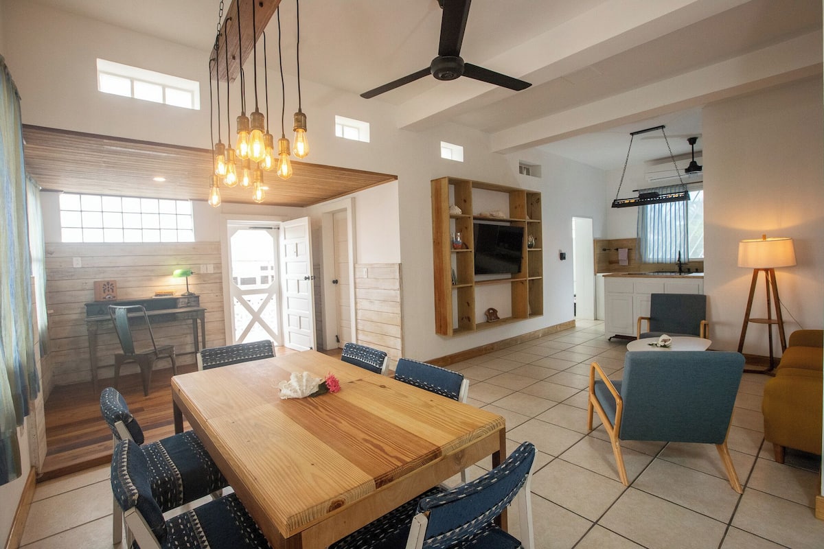Amplia sala de estar con una mesa de comedor de madera, sillas tapizadas en azul y un ventilador de techo.