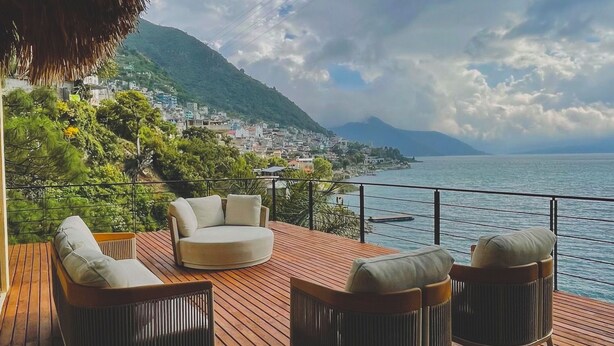 A wooden deck with outdoor seating, overlooking a coastal town and the sea. - Lakeview on the Rocks (San Antonio Palopó)