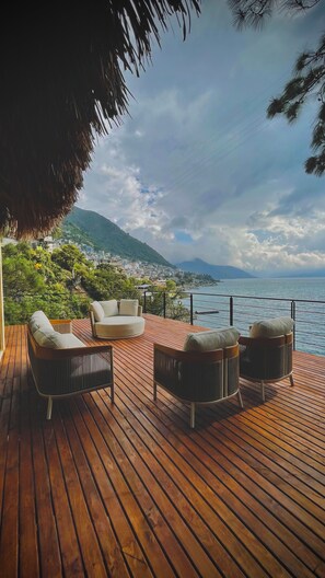 A wooden deck with outdoor seating, overlooking a coastal town and the sea. - Lakeview on the Rocks (San Antonio Palopó)