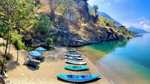 A beach with kayaks lined up, a row of sun loungers, and a clear view of the water and mountains in the background. - Lakeview on the Rocks (San Antonio Palopó)