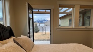 A bedroom with a large bed, a window with a view of mountains, and a door leading outside. - Modern Dog Friendly Paradise Valley Home near Yellowstone NP & Chico Hot Springs (Pray)